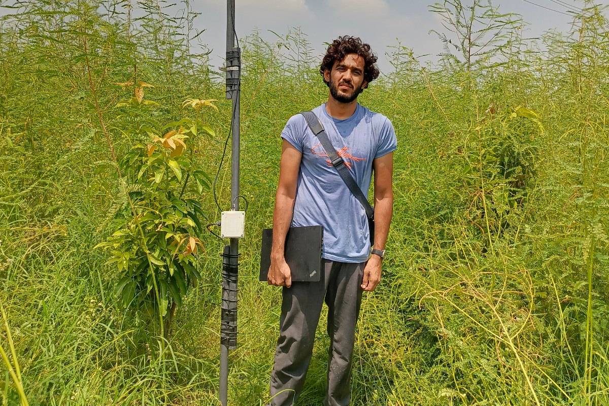 Company Overview Field engineer with a laptop standing beside a tall WaterSense telemetry mast in a green fodder plot